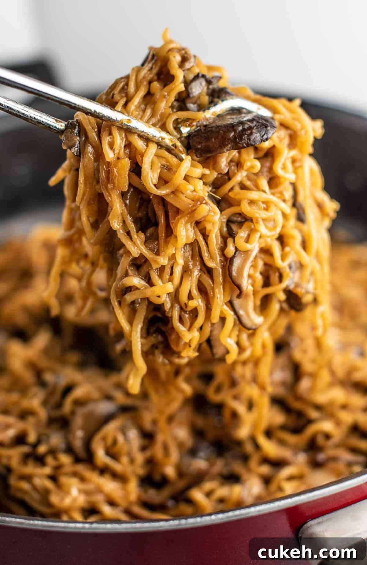 ramen noodles with mushrooms being pulled with tongs from a pan