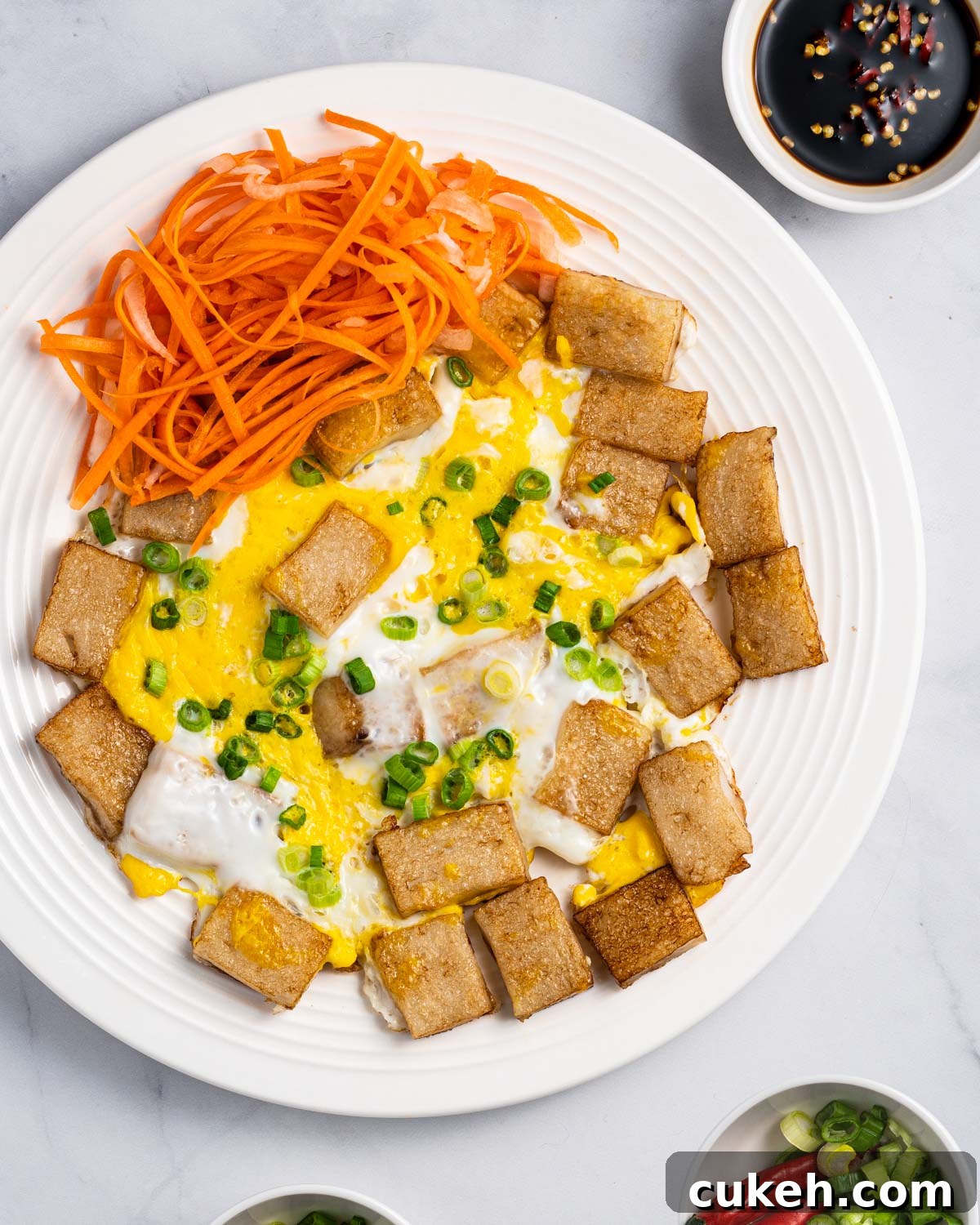 Plate of bot chien (Vietnamese fried rice cakes) with sides of pickled carrots and daikon, dipping sauce, chopped scallions, and red peppers.