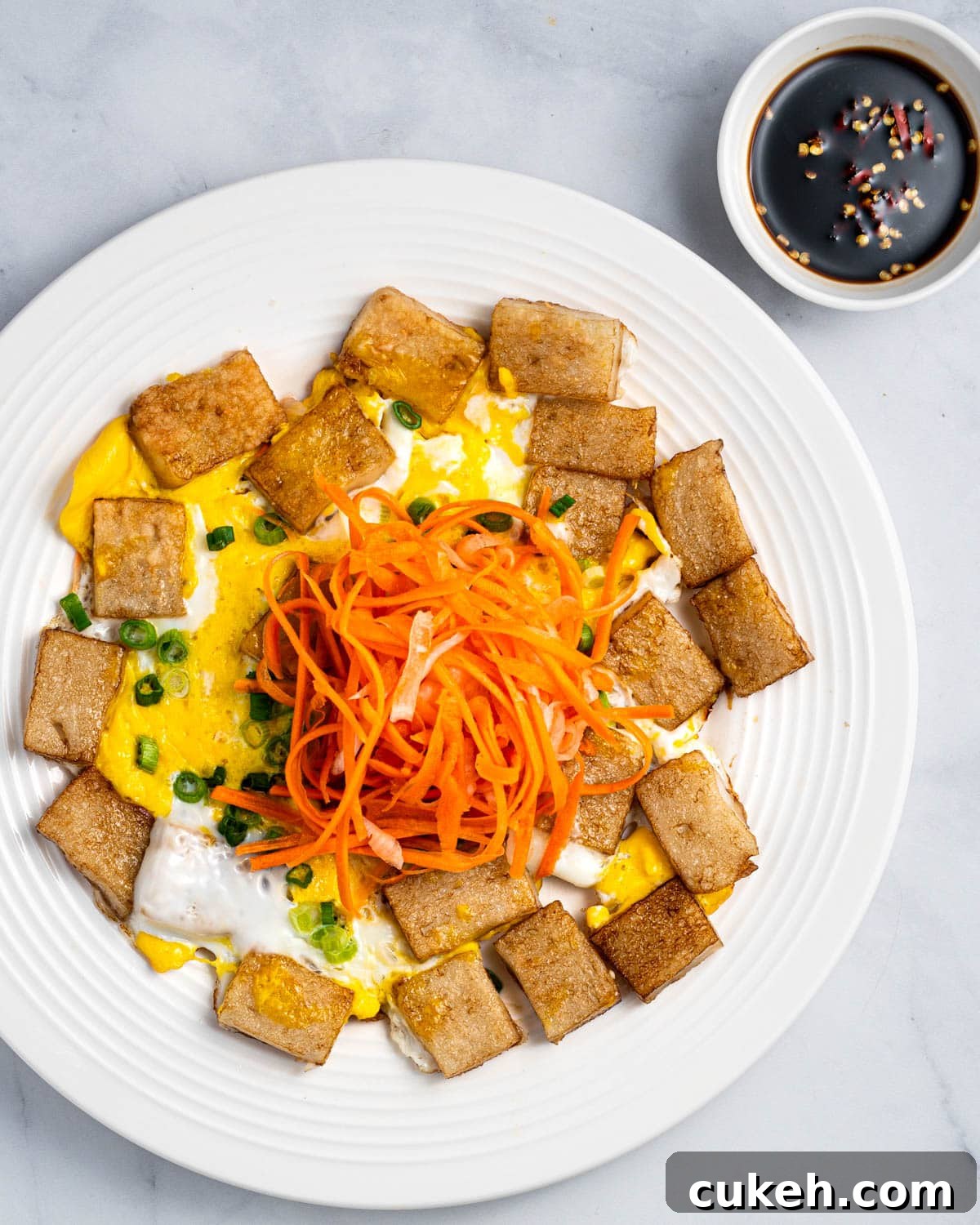 A plate of bot chien with pickled carrots and daikon on top and dipping sauce on the side.