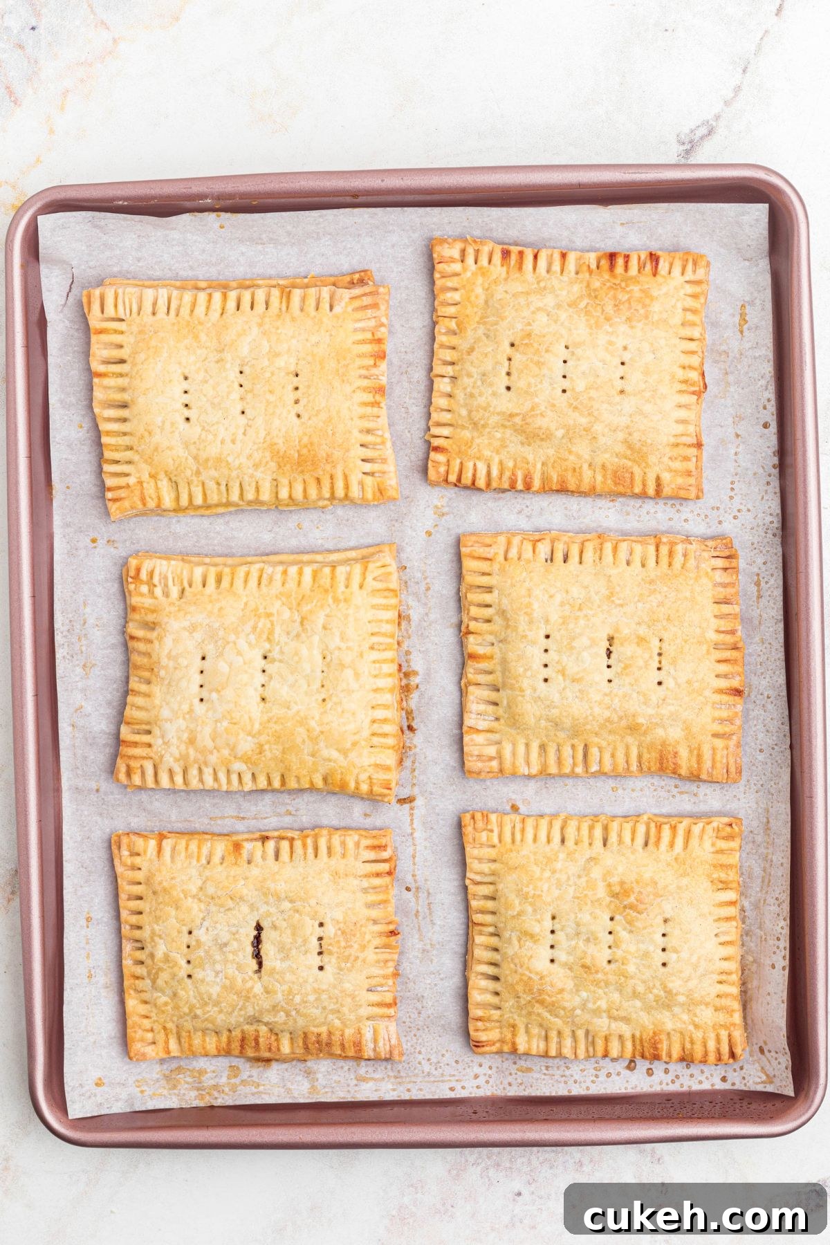 Golden baked pastries, on a pink baking sheet, lined with parchment paper. 