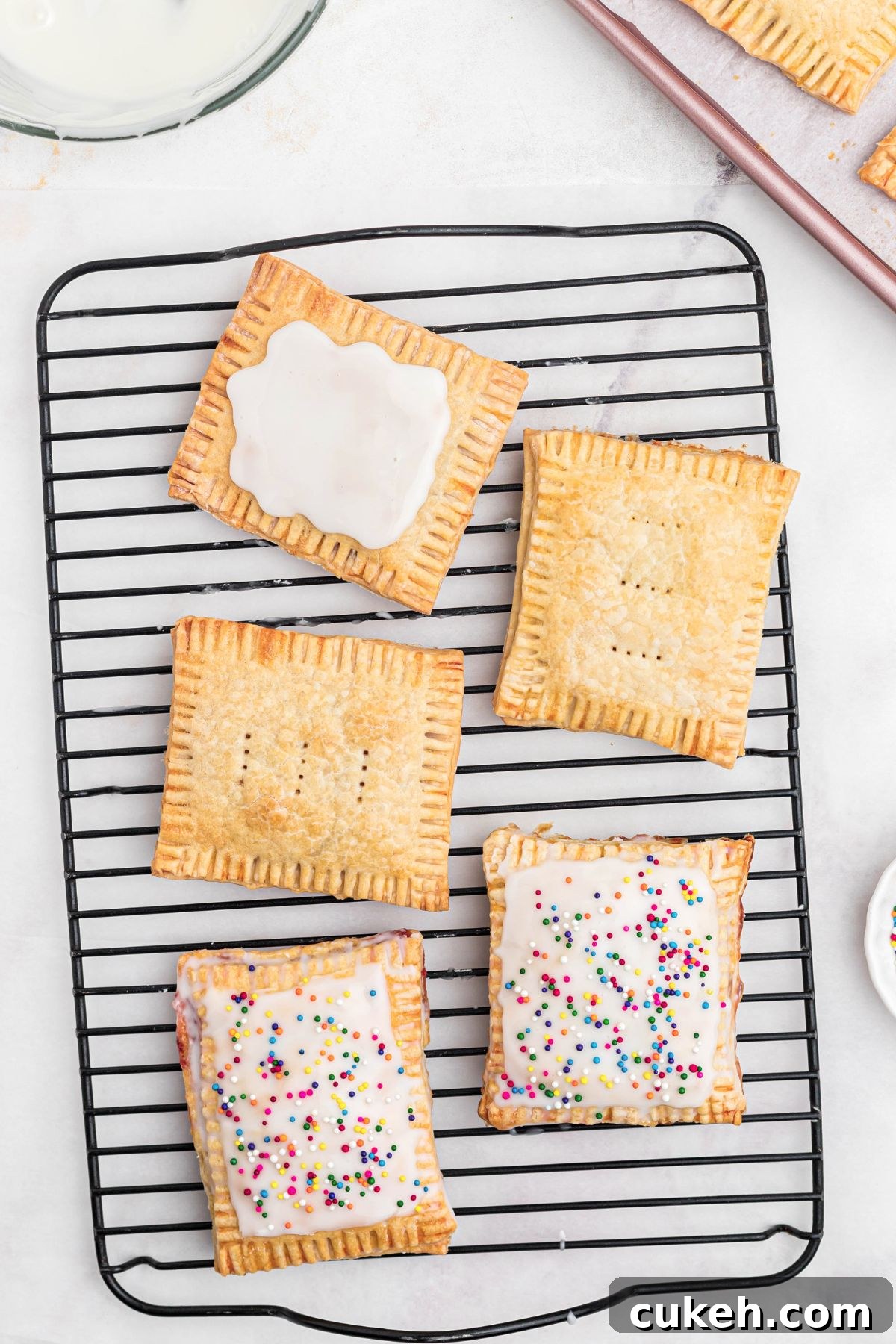 Baked pastries being topped with white icing and sprinkles, on a cooling rack. 