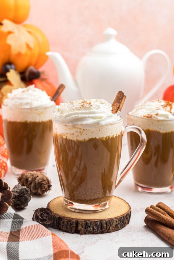 Cups of coffee topped with whipped cream, in front of white pot, on a marble board.