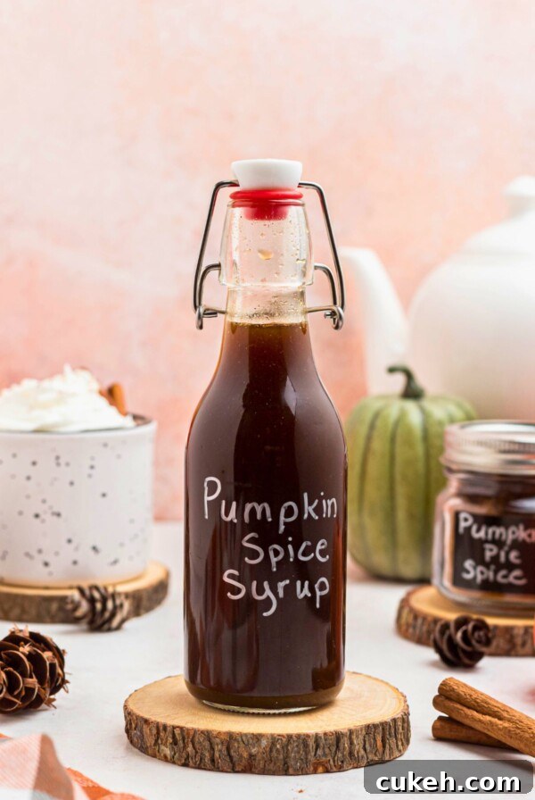 Bottle of pumpkin spice syrup on a small wooden coaster next to a cup of coffee, on a marble table.