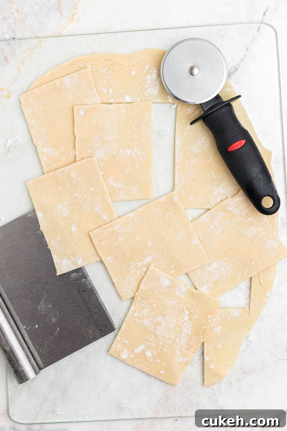 Rolled out pie dough, on a marble table, cut into small squares by a pizza cutter. 