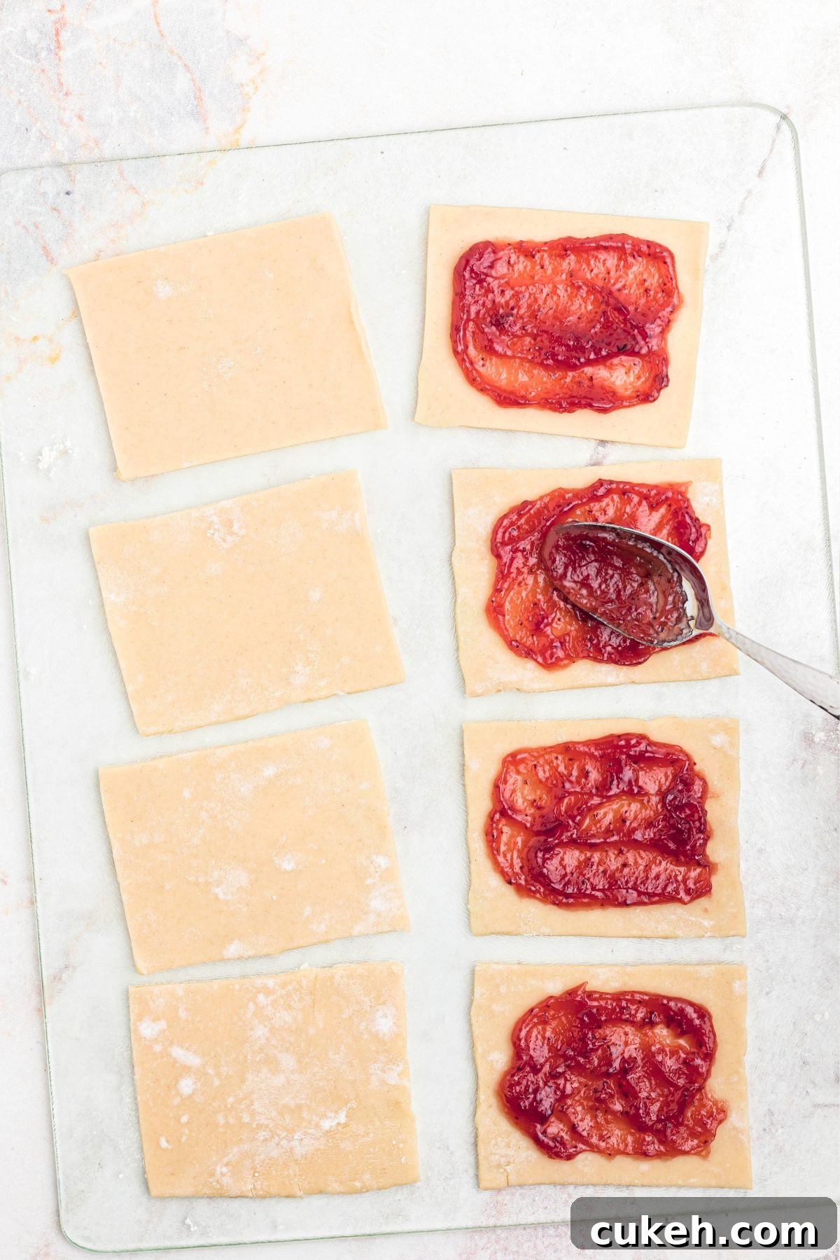 Jam being added by the spoonful to pie crust dough that has been cut into squares. 