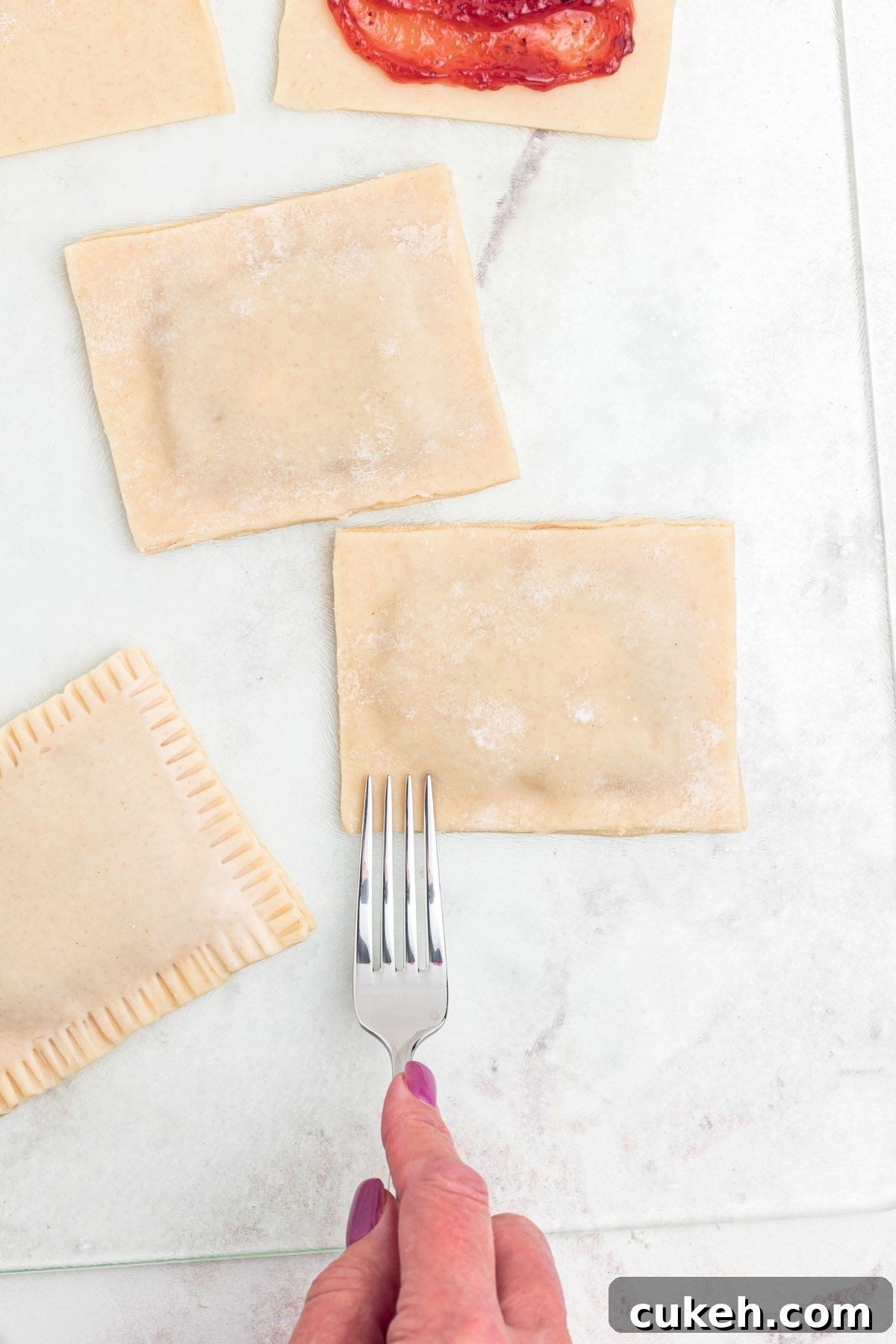 Crusts being filled with jam, and then being sealed with a fork being pressed into the edges. 