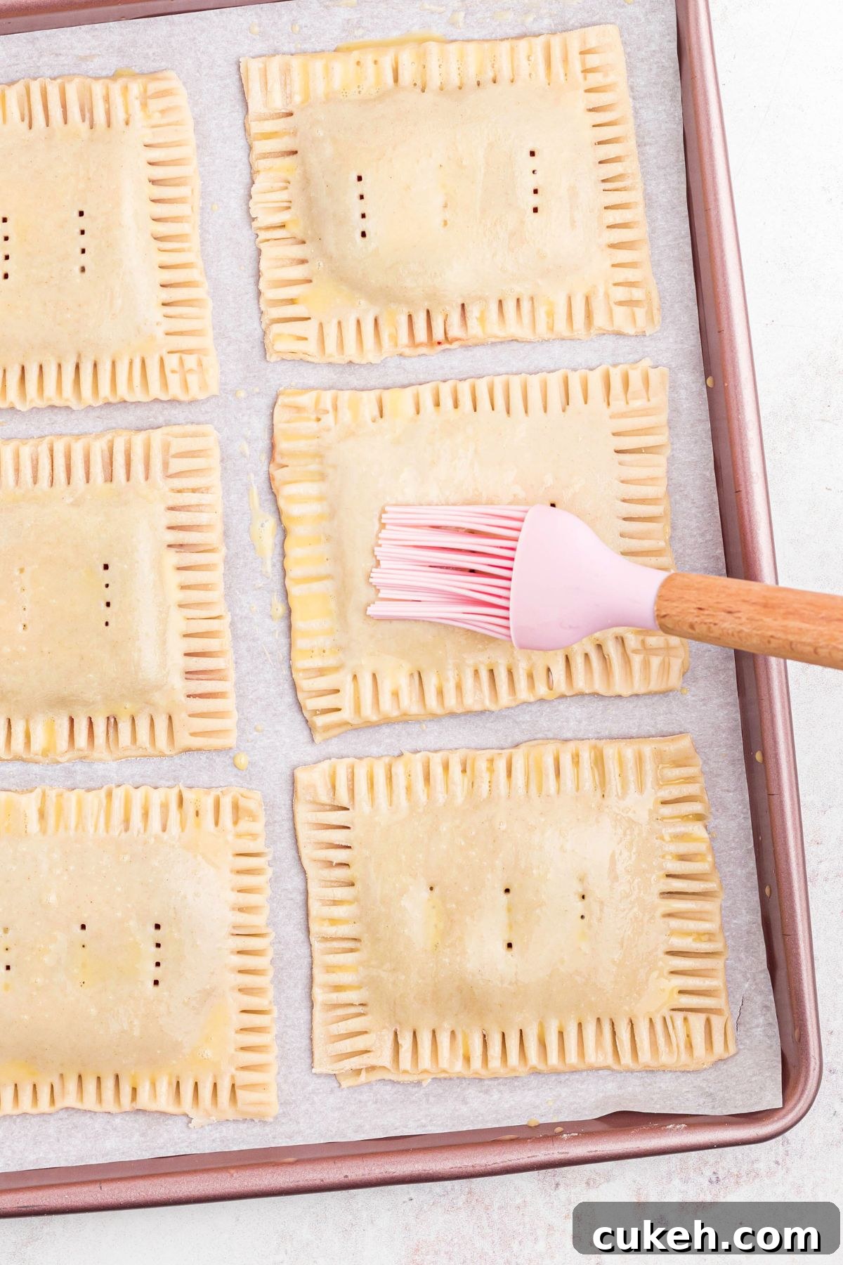 Pastries filled with jam, being brushed with an egg wash before being baked in the oven.