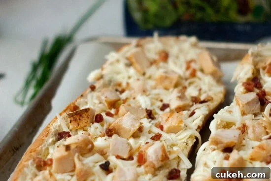Garlic bread with with shredded mozzarella cheese, cooked chicken, and crumbled bacon on a baking sheet with parchment paper.