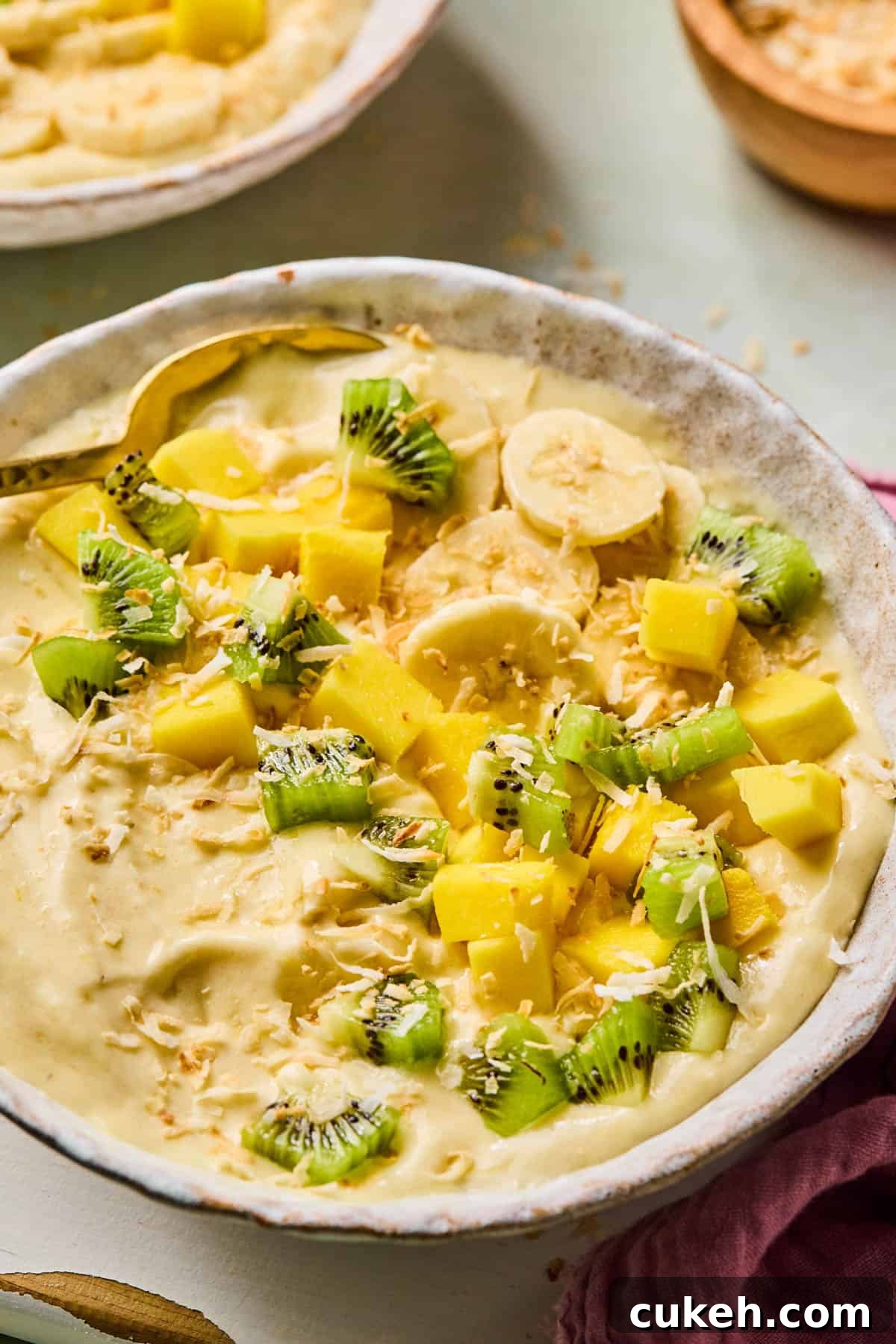 spoon dipped into a coconut smoothie bowl topped with kiwi, banana, and mango slices