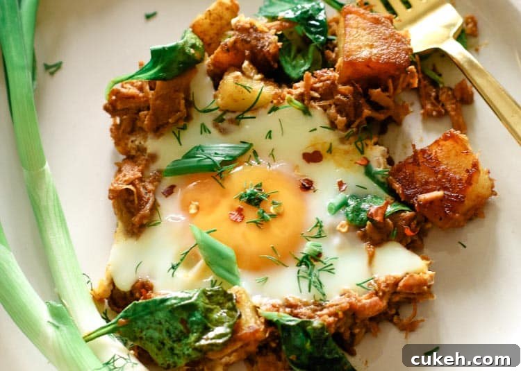 Breakfast pulled pork and potatoes hash on a white plate with green onions on the side.