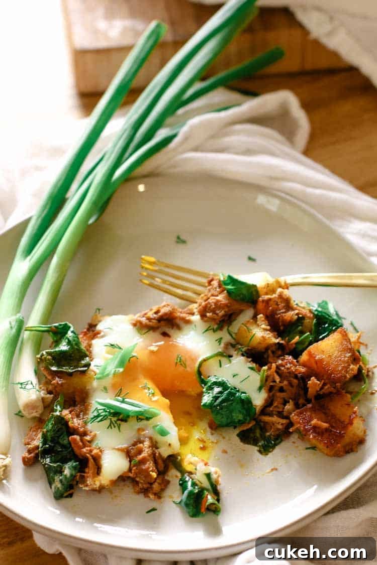 White plate with pulled pork, eggs, potatoes, spinach and garnishes for an easy skillet breakfast.