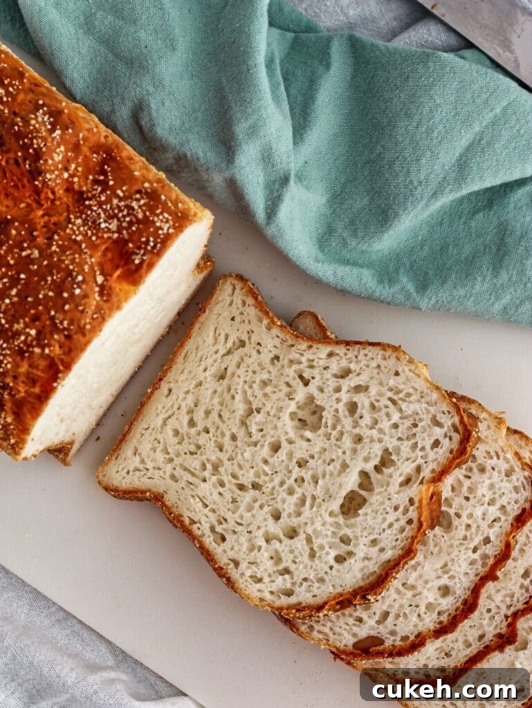 half sliced loaf of gluten free English muffin bread on white cutting board with teal cloth napkin.  