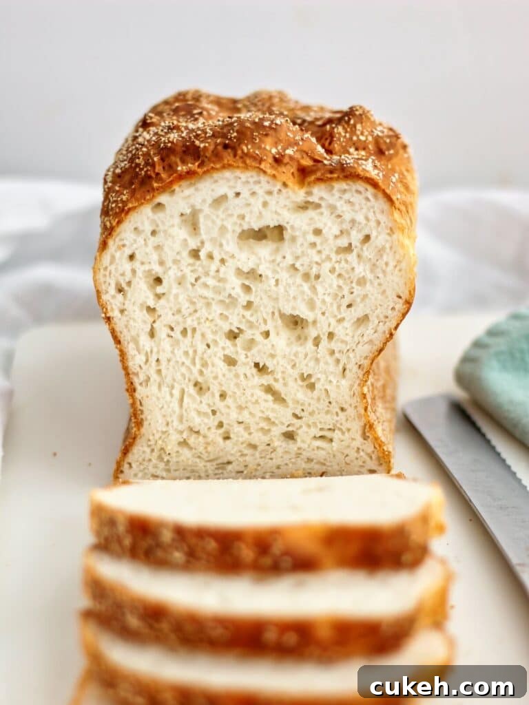 front view of half sliced loaf of English muffin bread on white plastic cutting board.
