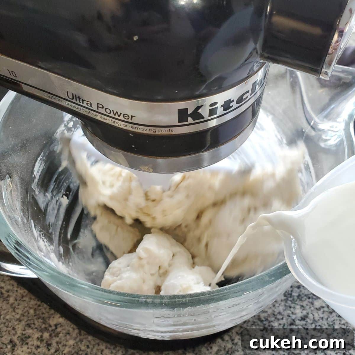 pouring milk into dry ingredients in glass stand mixer bowl.