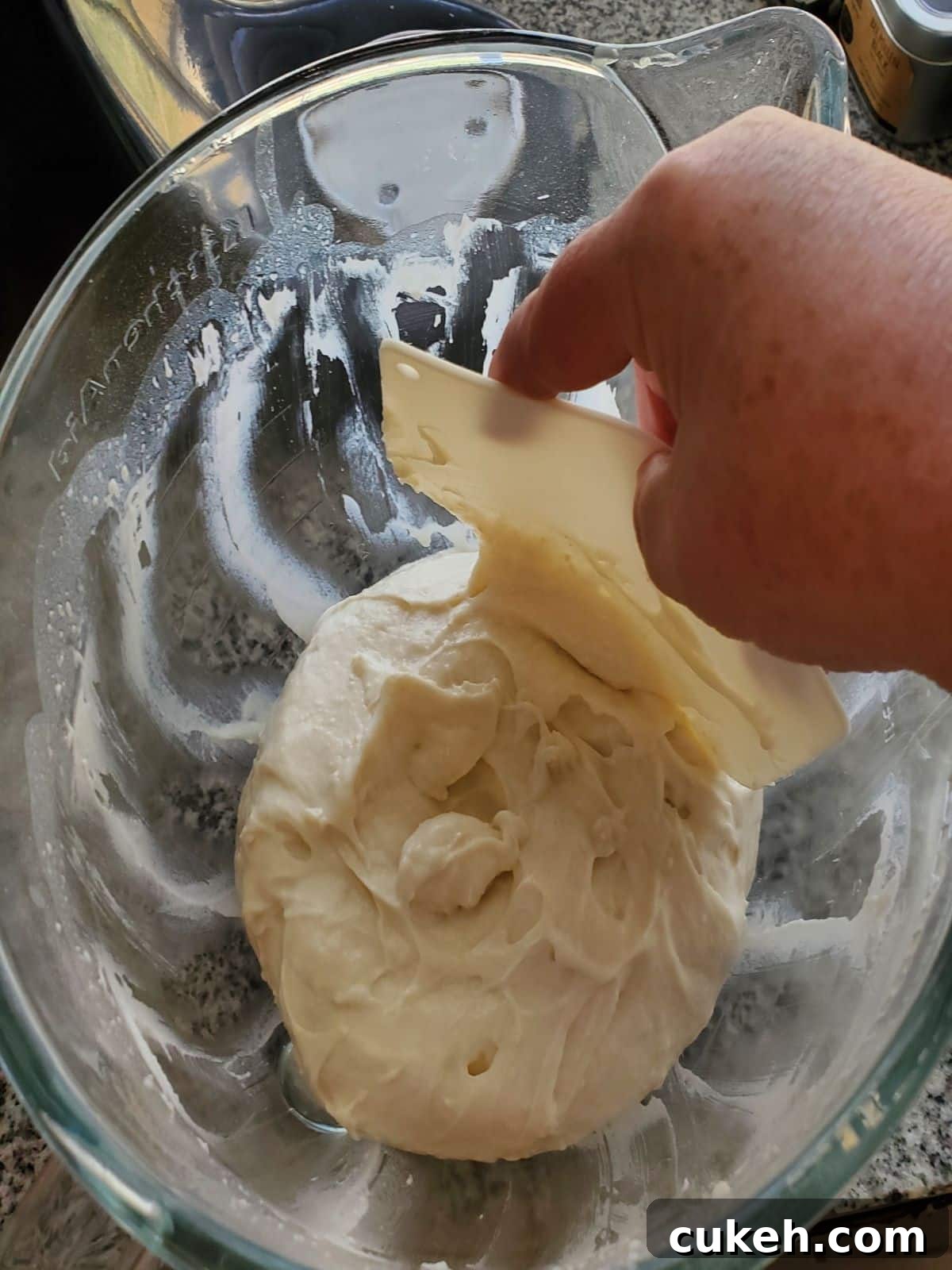 scraping dough into center of glass bowl with white flexible bowl scraper.