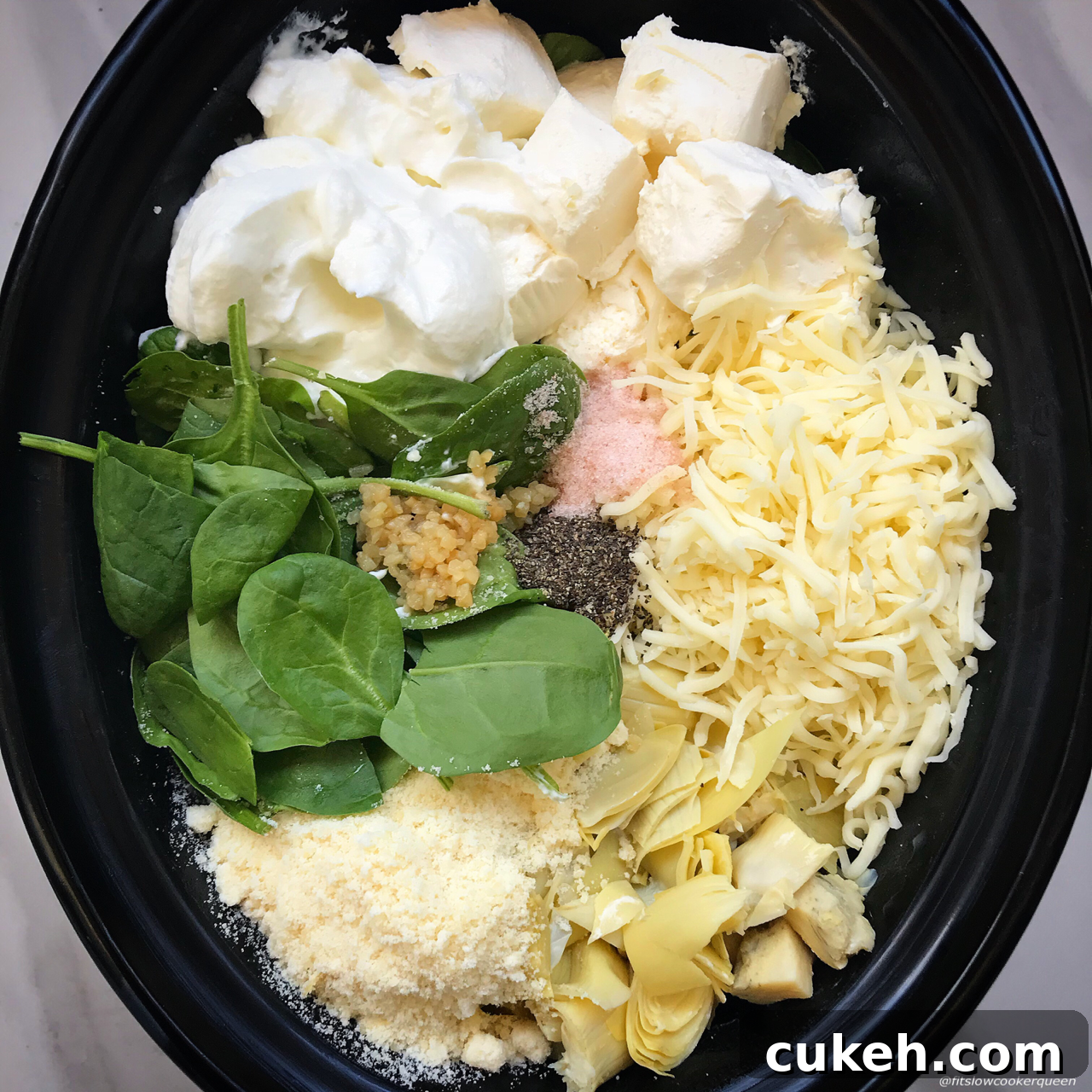 overhead shot of uncooked Crockpot Spinach Artichoke Dip in a black slow cooker