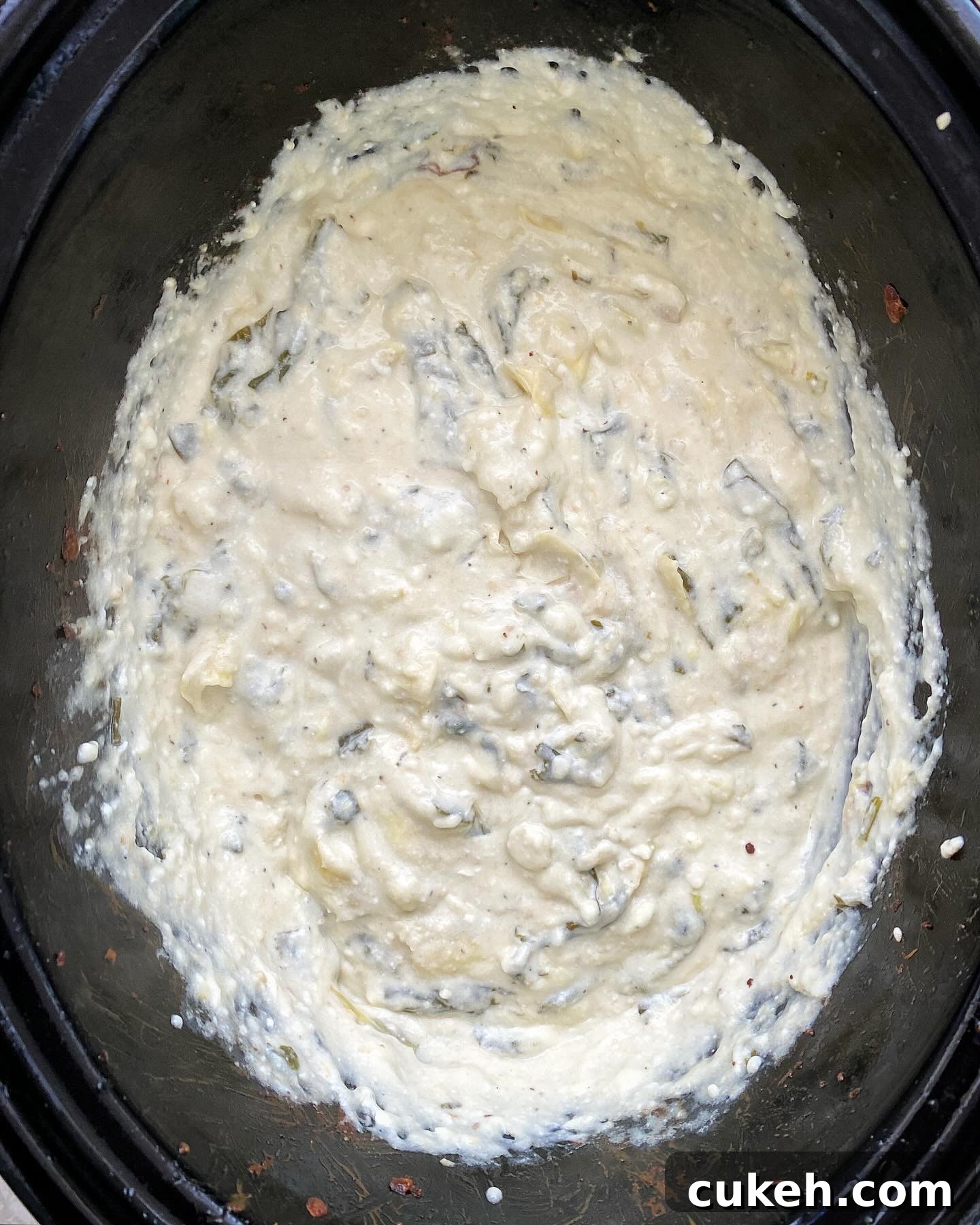 overhead shot of cooked Crockpot Spinach Artichoke Dip in a black slow cooker