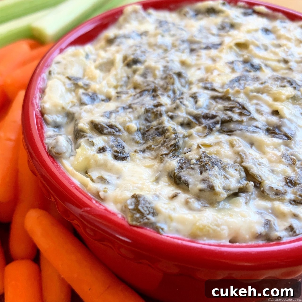 Creamy Slow Cooker Spinach Artichoke Dip Recipe 6 overhead shot of cooked Crockpot Spinach Artichoke Dip in a red bowl garnished with baby carrots and celery sticks