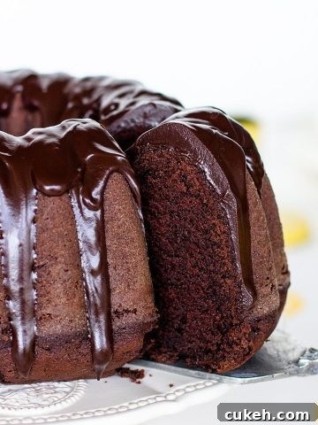 Cake server with slice being pulled out of glazed chocolate bundt cake, white background.