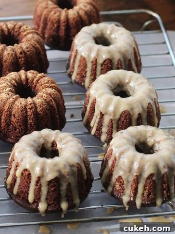 Two rows of glazed mini chocolate cakes on a wire rack with parchment underneath.