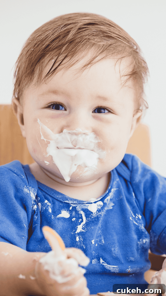 Little Boy Feeding Himself Yogurt with Messy Face and Shirt