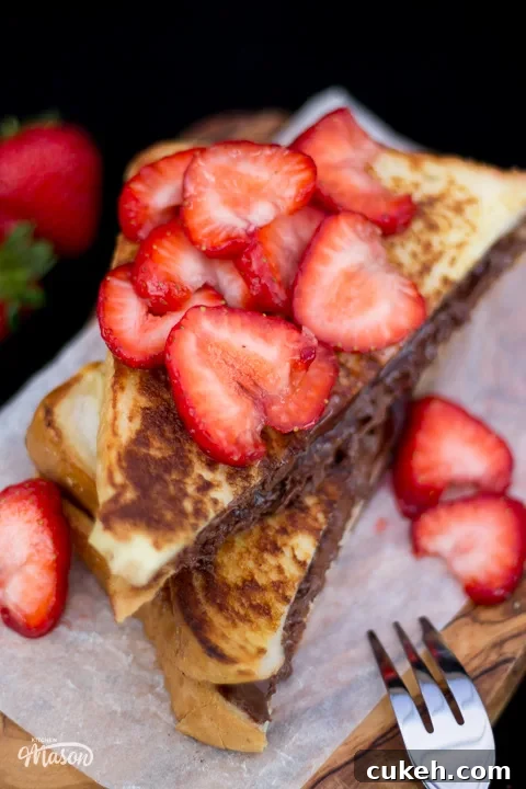 Sliced strawberries on top of Nutella French toast on a wooden board with a fork.