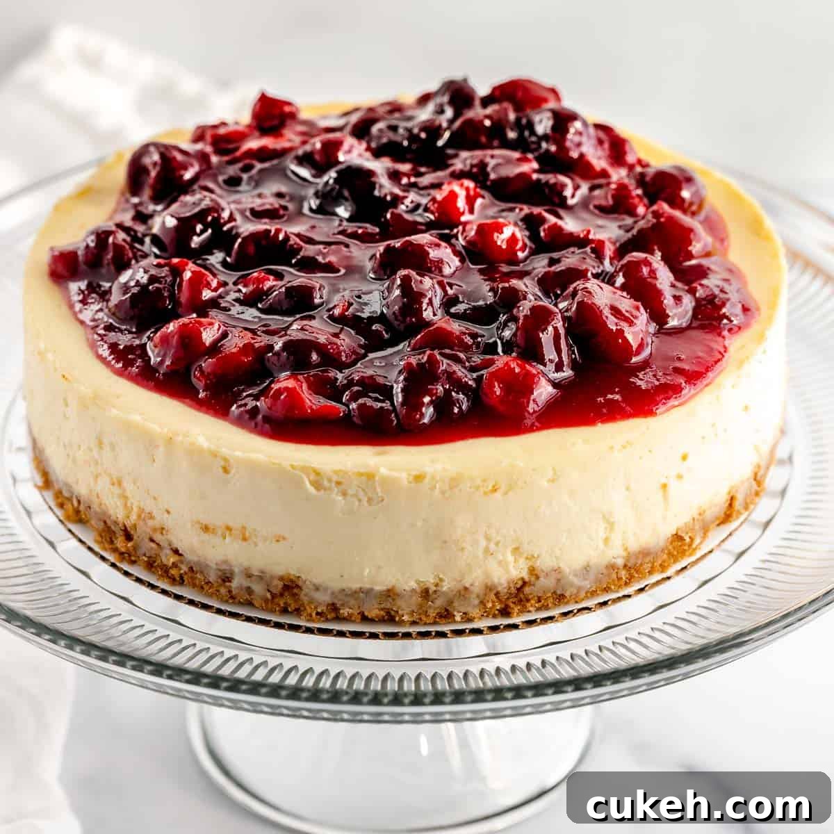 Cherry cheesecake with graham cracker crust on a cake stand.