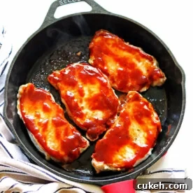 A cast iron pan with four cooked bbq pork chops in it.