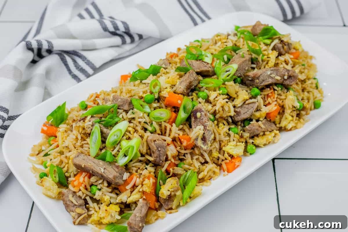 Steak fried rice on a white platter on white tiles with striped cloth on the side.