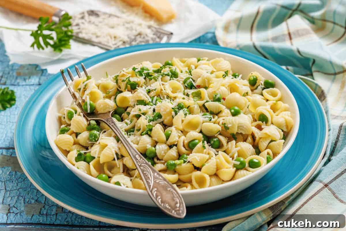 A bowl of pasta and peas with a fork, grater, and cheese on the side.