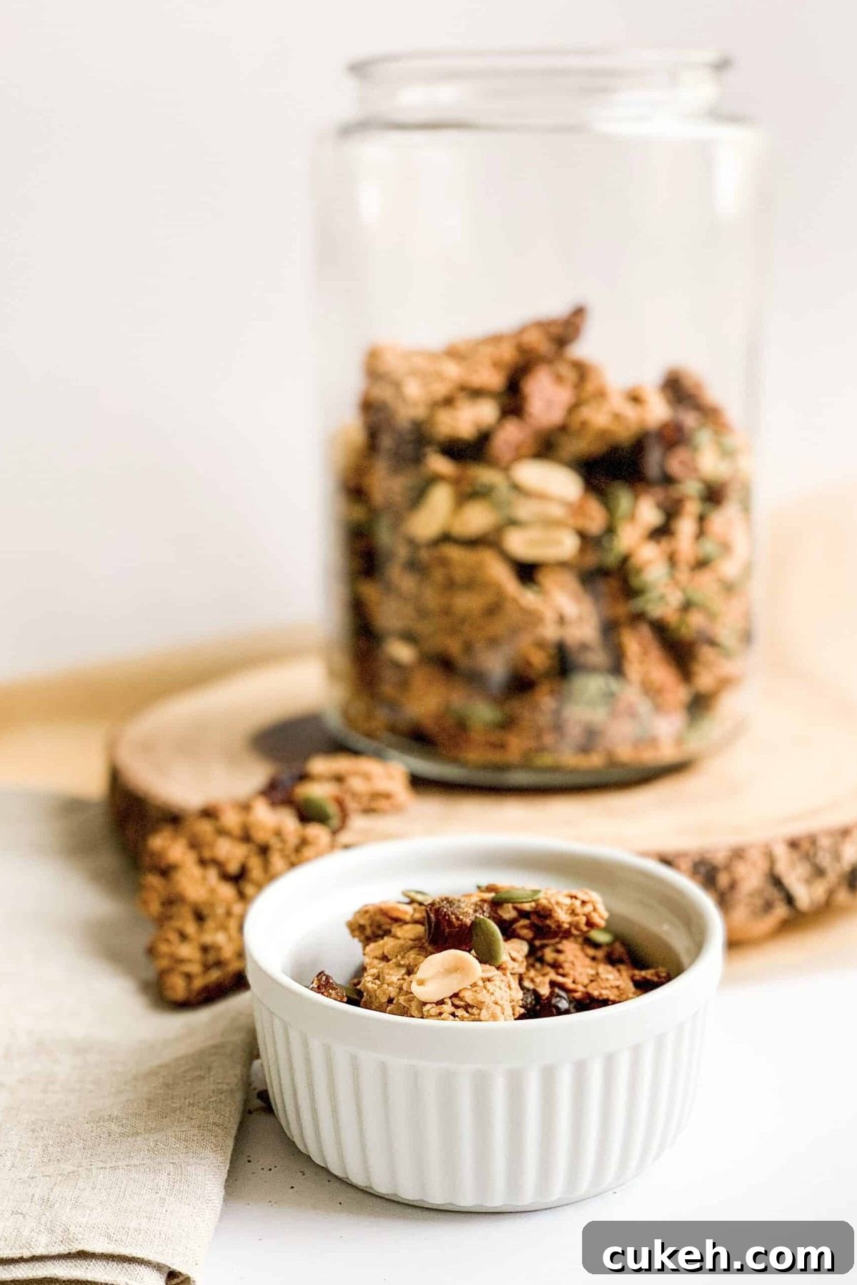 Jar of crunchy peanut butter granola with peanuts, pepitas and chopped dates, sitting on decorative wooden platter