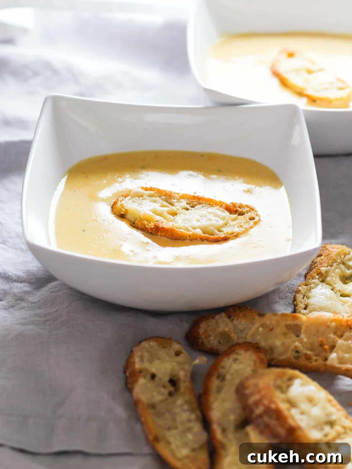 Square white bowl with cheese soup and a large crouton on top.