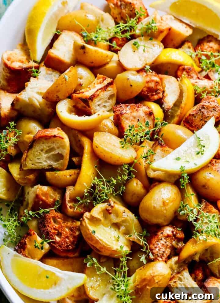 A white platter filled with sheet pan chicken dinner including lemons, potatoes, and croutons.