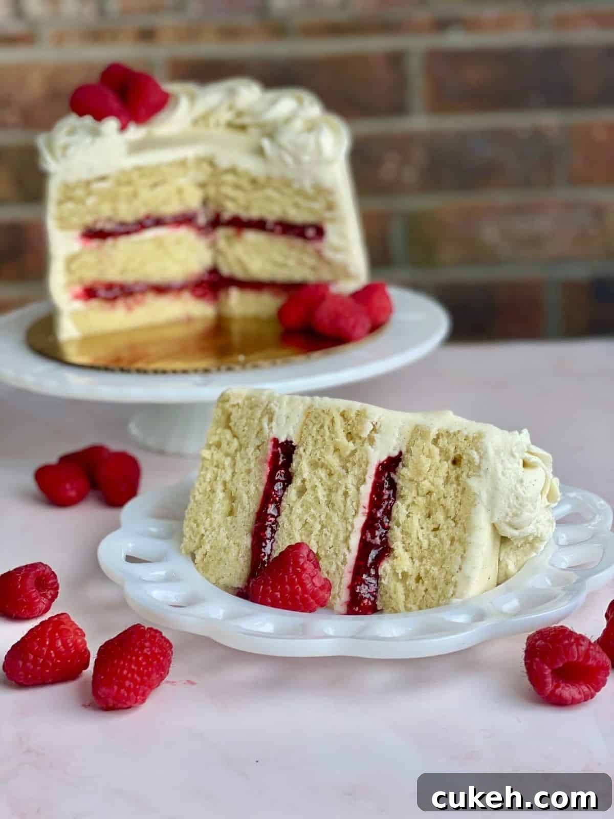 A layered cake with Raspberry Cake Filling with the remaining cake on a cake pedistal.