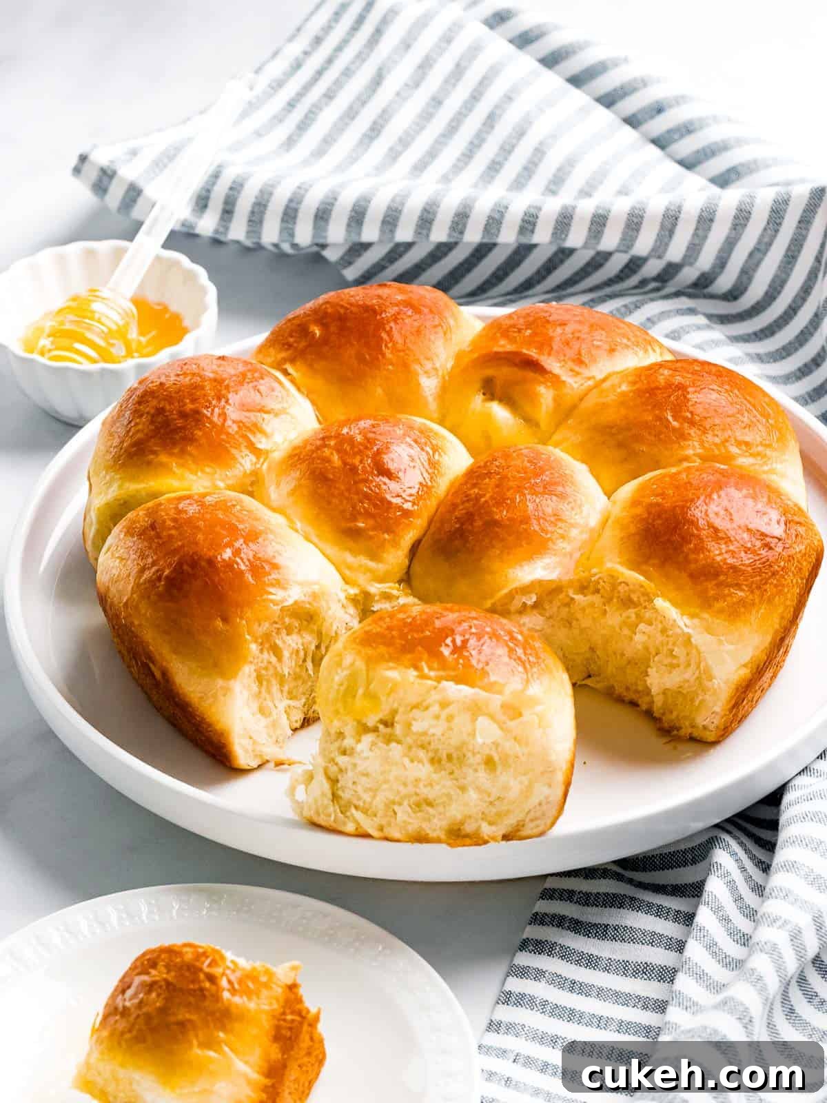 Soft buttery brioche rolls baked until golden brown next to a small bowl of honey.